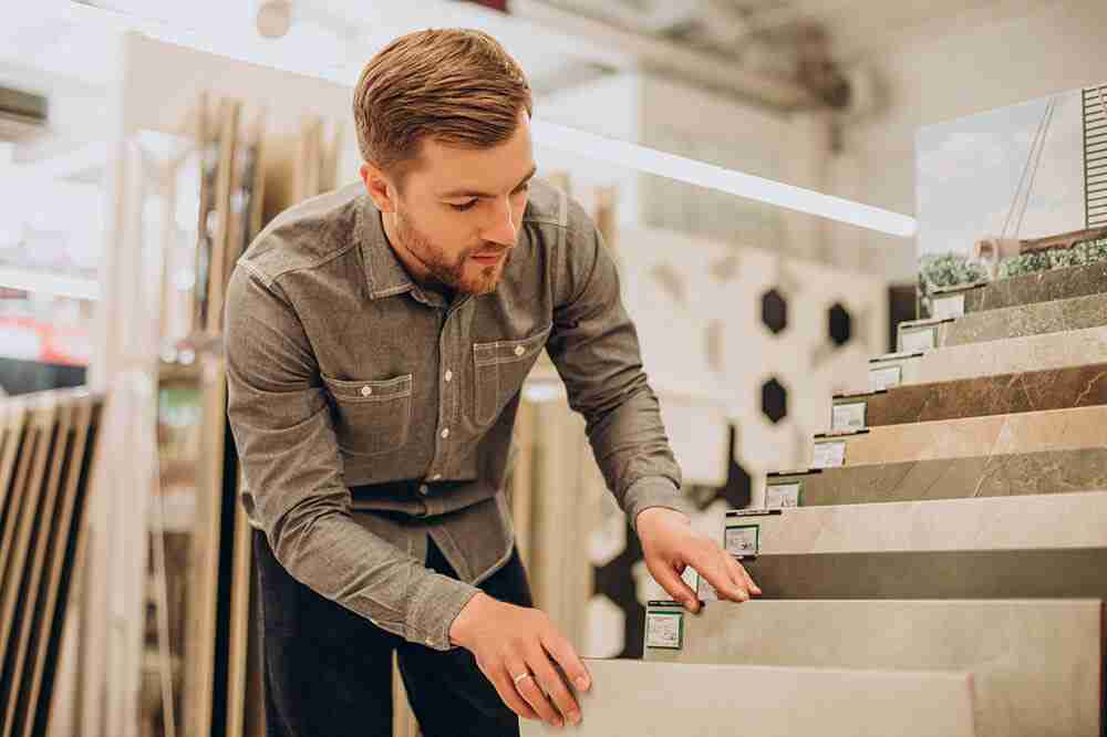 young-man-choosing-tiles-at-building-market-scaled